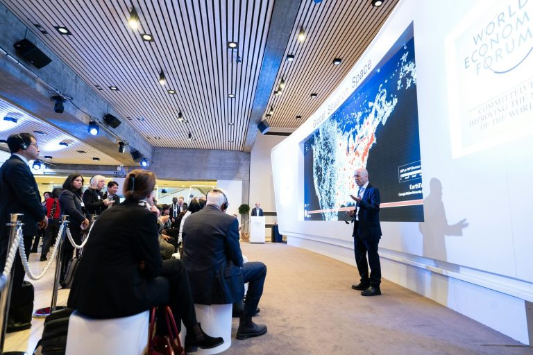 A speaker on stage near a screen at a global economic forum, representing event and corporate video editing services by BestEditLab.