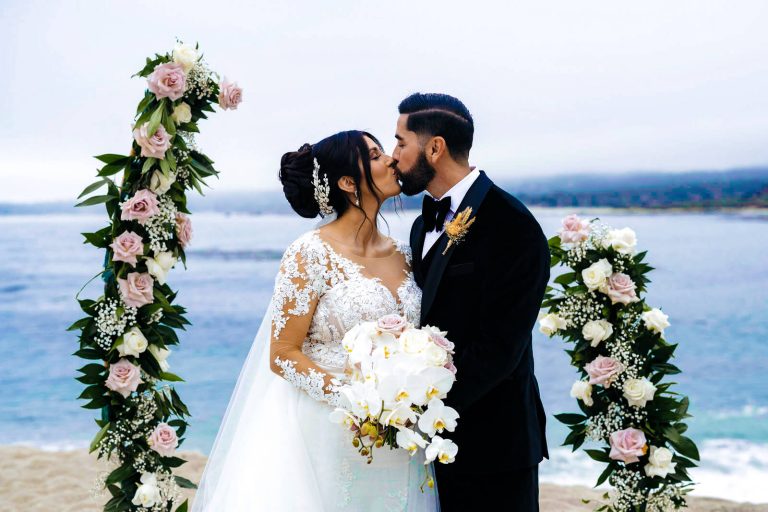 A couple kissing by a floral altar on the beach during their wedding ceremony, edited by BestEditLab as part of outsourced wedding video editing services.